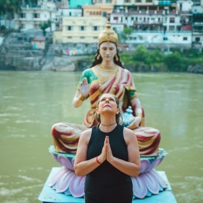 A woman praying beside a Hindu goddess statue by a river in Rishikesh, India.